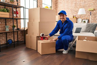 Young hispanic man worker packing package at new home