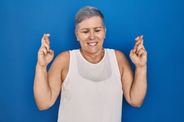 Orta yaşlı, beyaz bir kadın mavi arka planda durup umut ve gözleriyle gülümseyerek işaret ediyor. Şans ve batıl inançlar. 