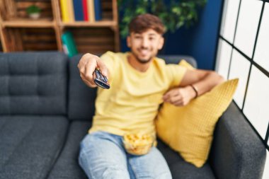 Genç Arap adam evde film izlerken patates kızartması yiyor.