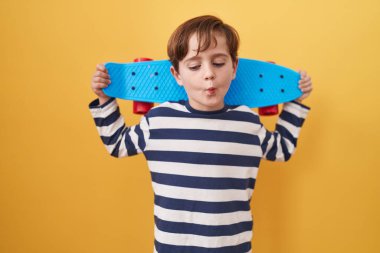 Küçük beyaz çocuk sarı arka planda paten kayıyor. Ağzı ve şaşı gözleriyle balık suratı yapıyor. Deli ve komik.. 