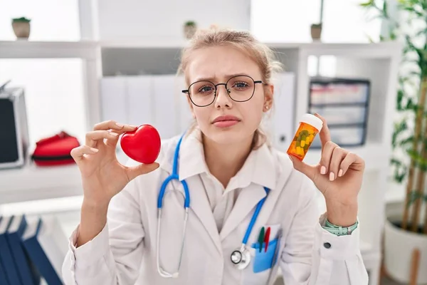 Jovem Mulher Médica Caucasiana Segurando Pílulas Expressão Sem Noção Cardíaca — Fotografia de Stock