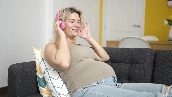 若いです妊娠中の女性リッスンTo音楽嘘上のソファホーム — ストック写真