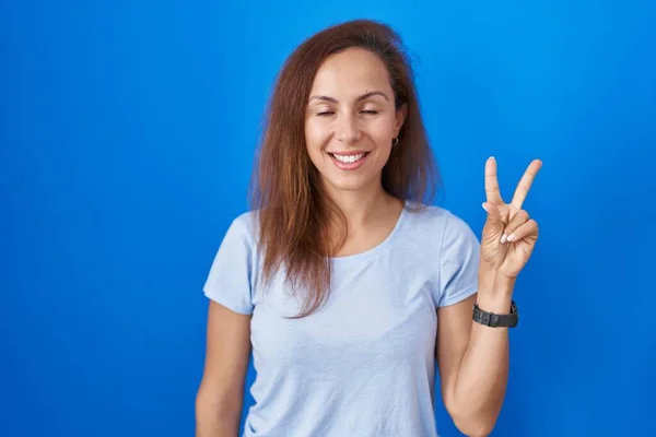 布鲁内特的女人站在蓝色的背景上 用二号手指指指着 脸上带着自信和快乐的笑容 — 图库照片