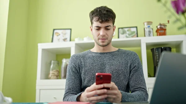 Hombre Hispano Joven Usando Teléfono Inteligente Portátil Sentado Mesa Comedor —  Fotos de Stock