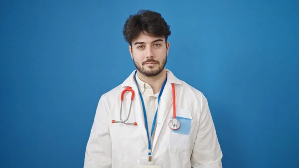 Fiatal Spanyol Férfi Orvos Áll Komoly Kifejezés Izolált Kék Háttér — Stock Fotó