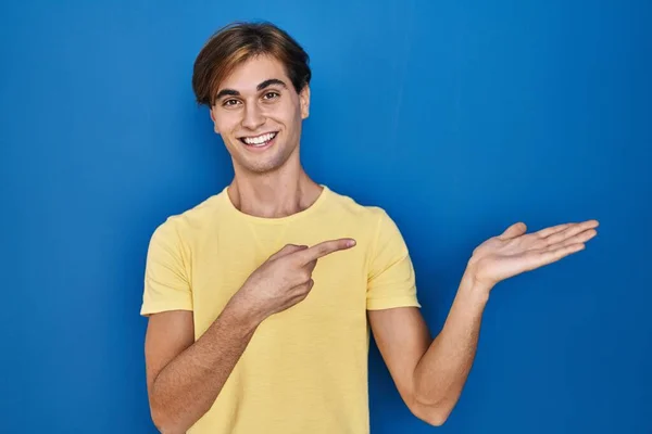 Νεαρός Άνδρας Στέκεται Πάνω Από Μπλε Φόντο Έκπληκτος Και Χαμογελώντας — Φωτογραφία Αρχείου
