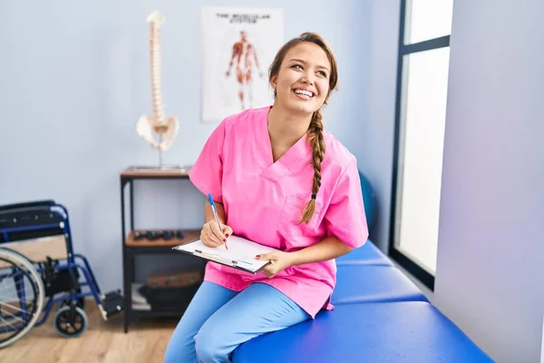 Jovem Bela Mulher Hispânica Fisioterapeuta Sorrindo Escrita Confiante Documento Clínica — Fotografia de Stock