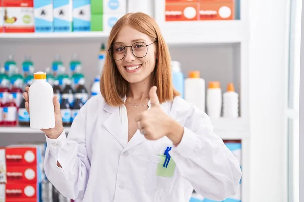 Νεαρή Κοκκινομάλλα Γυναίκα Που Εργάζονται Φαρμακείο Κρατώντας Αντηλιακό Χαμογελώντας Χαρούμενος — Φωτογραφία Αρχείου