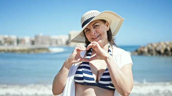 Латиноамериканка Средних Лет Туристка Бикини Делает Сердечный Жест Руками Пляже — стоковое фото
