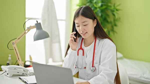 年轻的中国女医生在诊所用手提电脑用智能手机交谈 — 图库照片