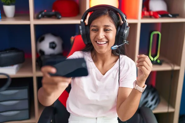 幸せな笑顔で達成を祝うスマートフォンでビデオゲームをプレイし 手を上げて勝者の表情を持つ若いヒスパニック女性 — ストック写真