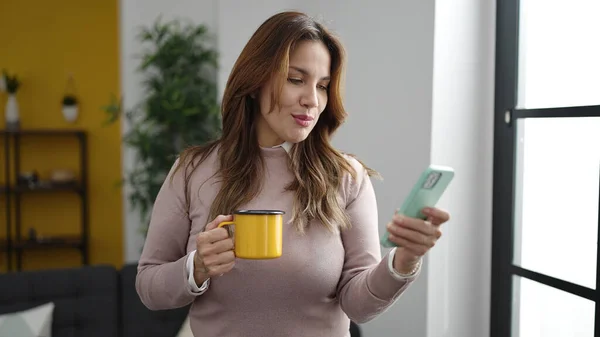 Young Beautiful Hispanic Woman Using Smartphone Drinking Coffee Home — Fotografia de Stock