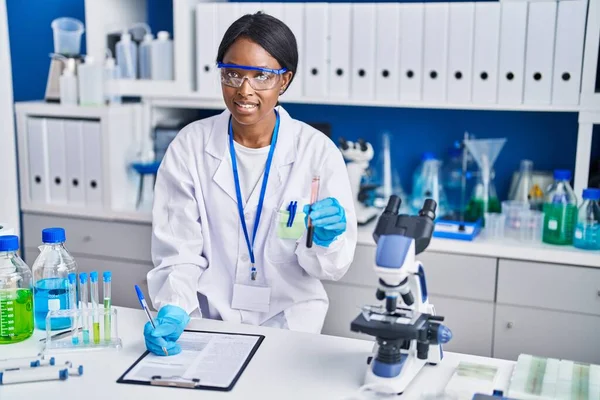 若いアフリカ系アメリカ人女性科学者は 実験室で血液検査管を保持する文書に書きます — ストック写真