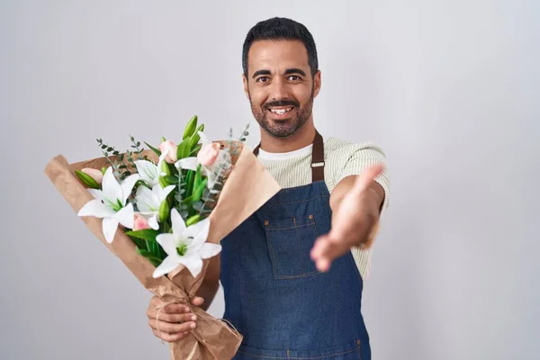 Hispanic man with beard working as florist smiling friendly offering handshake as greeting and welcoming. successful business.