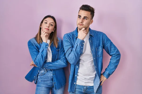 Young Hispanic Couple Standing Pink Background Hand Chin Thinking Question — 图库照片