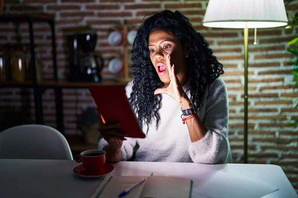 stock image Middle age hispanic woman using touchpad sitting on the table at night hand on mouth telling secret rumor, whispering malicious talk conversation 