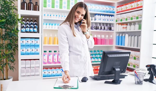 Young Beautiful Hispanic Woman Pharmacist Talking Smartphone Writing Document Pharmacy — Stock Fotó