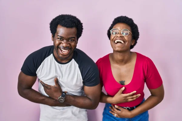 一对年轻的非洲裔美国夫妇站在粉红的背景上 笑得很开心 笑得很大声 因为他们手拉手在身上开了一个可笑的疯狂玩笑 — 图库照片