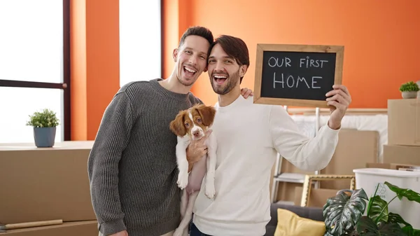 Two men couple hugging each other holding dog and blackboard at new home