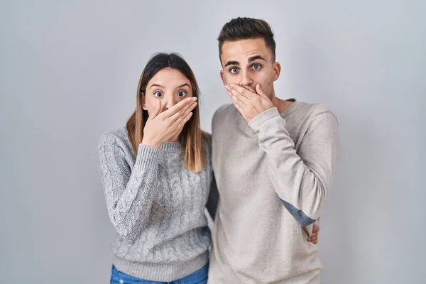 若いヒスパニック系のカップルが白い背景の上に立ってミスのために手で口をカバーショックを受けた 秘密の概念 — ストック写真