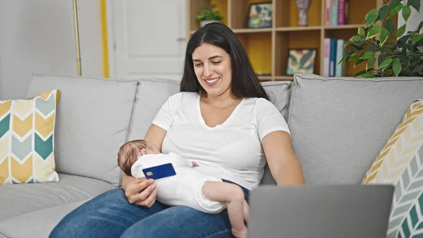 自宅でオンラインショッピングをしている赤ちゃんを抱えているソファに座っている母と赤ちゃんの娘 — ストック写真