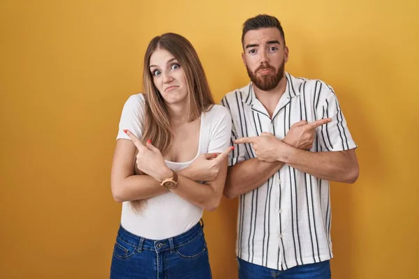 Sarı Arka Planda Duran Genç Çift Iki Tarafı Parmaklarıyla Işaret — Stok fotoğraf