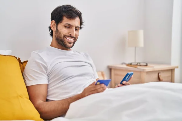 Young Hispanic Man Using Smartphone Credit Card Sitting Bed Bedroom — Stok fotoğraf