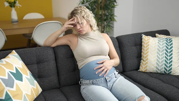 Mujer Embarazada Joven Sentada Sofá Con Expresión Estresada Tocando Vientre — Foto de Stock
