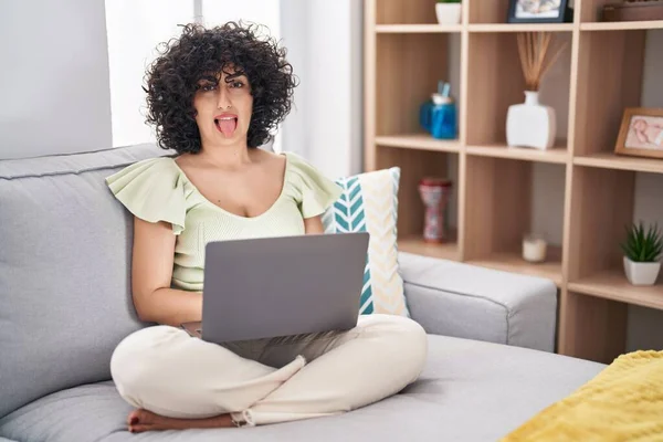 年轻的黑发女人 卷曲的头发 坐在家里沙发上 带着滑稽的表情伸出舌头 情感概念 — 图库照片