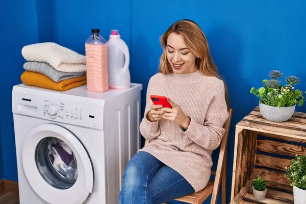 세탁실에서 세탁기를 기다리는 스마트폰을 사용하는 — 스톡 사진
