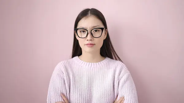 若いです中国の女性立っていますリラックスした式と腕交差ジェスチャー上の隔離されたピンクの背景 — ストック写真
