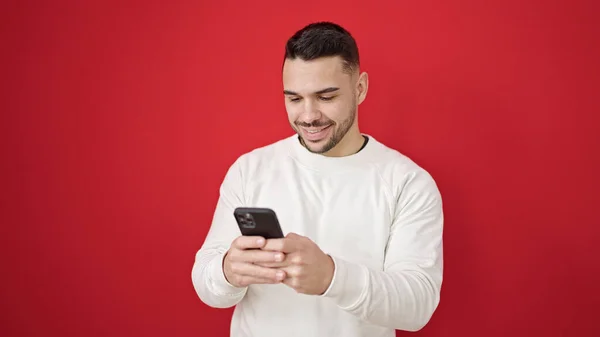 Hombre Hispano Joven Usando Teléfono Inteligente Sonriendo Sobre Fondo Rojo —  Fotos de Stock
