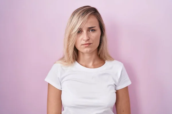 若いブロンドの女性ピンクの背景懐疑的で神経の上に立って 問題のために動揺を眉をひそめて 否定的な人 — ストック写真