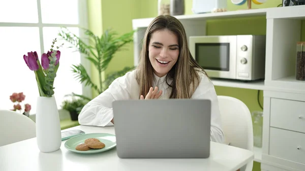 年轻美丽的惊慌失措的女人在饭厅用笔记本电脑吃饼干 — 图库照片