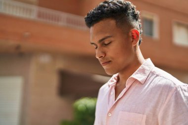 Young latin man with relaxed expression standing at street