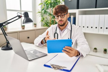 Young arab man wearing doctor uniform having video call at clinic