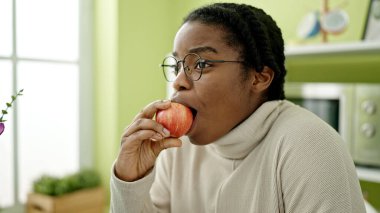 Afro-Amerikalı kadın yemek odasında elma yiyor.