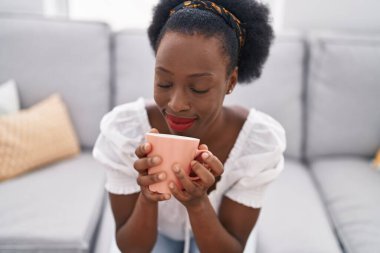 African american woman drinking coffee sitting on sofa at home