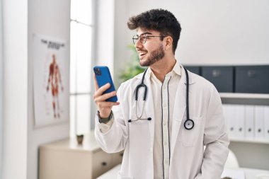 Klinikte akıllı telefon kullanan İspanyol doktor üniforması giyen genç adam.