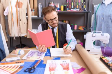 Orta yaşlı bir terzi atölyede defter okuyarak kitap çiziyor.