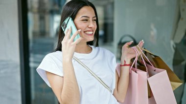 Genç, güzel İspanyol bir kadın elbise mağazasında akıllı telefondan konuşuyor.