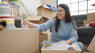 Young hispanic woman smiling confident unpacking cardboard box at new home