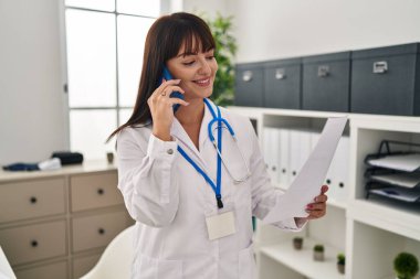 Genç, güzel İspanyol kadın doktor klinikte akıllı telefon okuyarak konuşuyor.