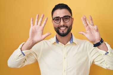 İspanyol genç adam iş kıyafetleri ve gözlük takıyor dokuz numaralı parmaklarıyla gösterip işaret ederken kendinden emin ve mutlu gülümsüyor.. 