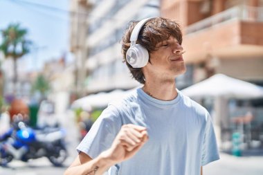 Young blond man listening to music and dancing at street
