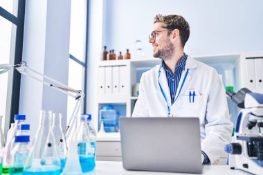 Genç bilim adamı laboratuvarda dizüstü bilgisayar kullanarak gülümsüyor.