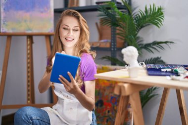 Young blonde woman artist smiling confident using touchpad at art studio