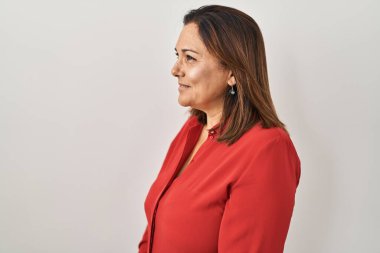 Beyaz arka planda dikilen Latin kökenli olgun bir kadın yan tarafa bakıyor, rahat poz veriyor kendine güvenen bir gülümsemeyle doğal bir yüz ifadesi sergiliyor.. 