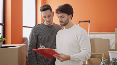 İki erkek, yeni evlerinde evrak okuyorlar.
