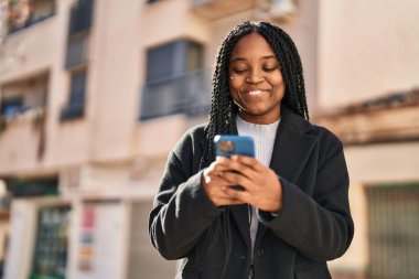 Afro-Amerikalı kadın sokakta akıllı telefon kullanarak kendine güveniyor.